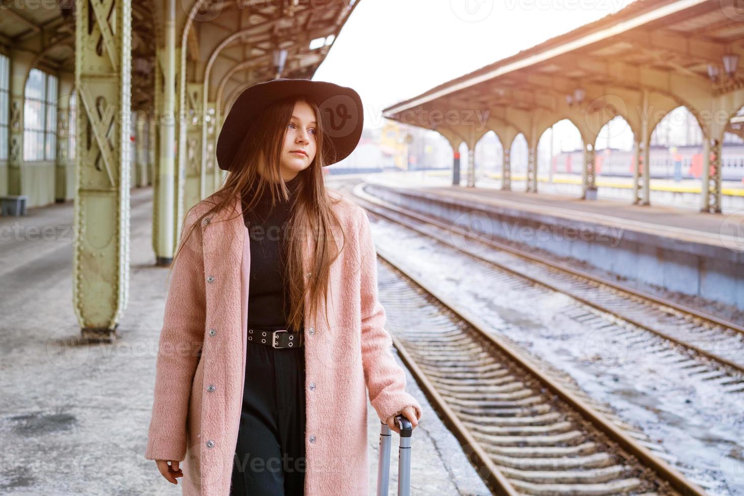 bella giovane donna turistica casual con una valigia in un cappotto rosa in attesa foto