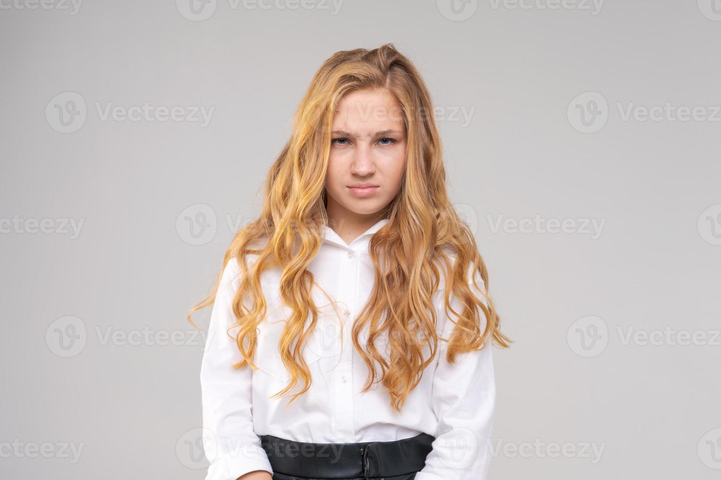 ritratto di giovane ragazza in camicia bianca con la faccia accigliata guarda la fotocamera foto