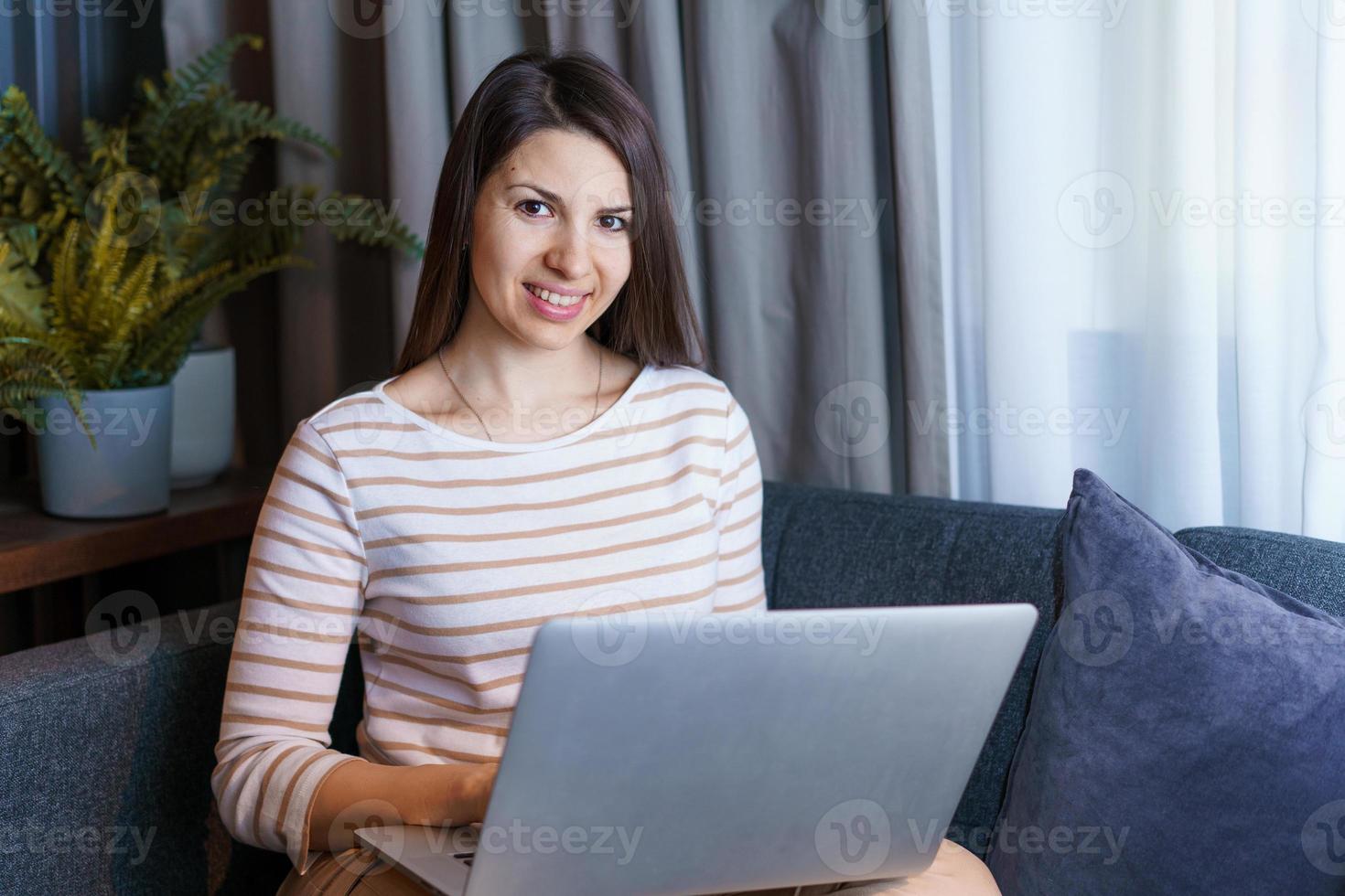 giovane donna seduta sul divano, che lavora al computer portatile, naviga in Internet o legge foto