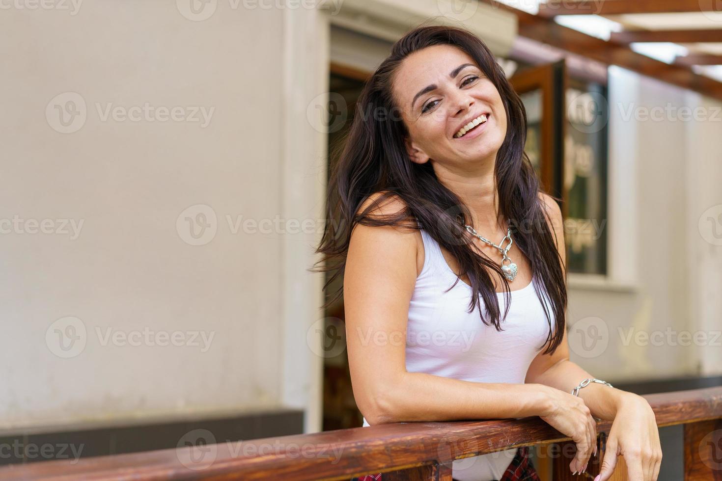 la giovane donna caucasica sta sorridendo in piedi sul portico vicino alla porta del negozio in casual foto