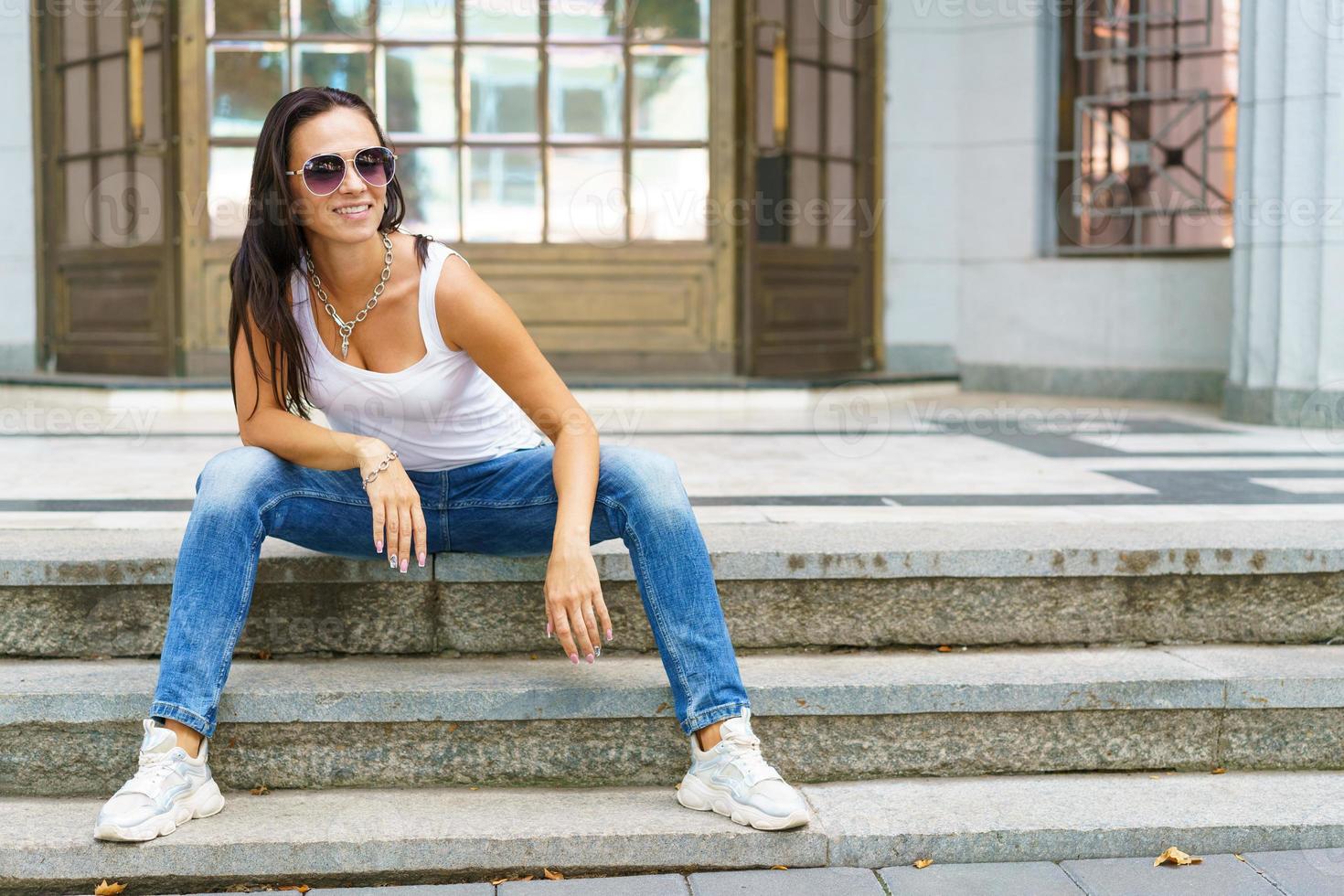ritratto di attraente donna felice seduta sulle scale in strada di città che indossa foto