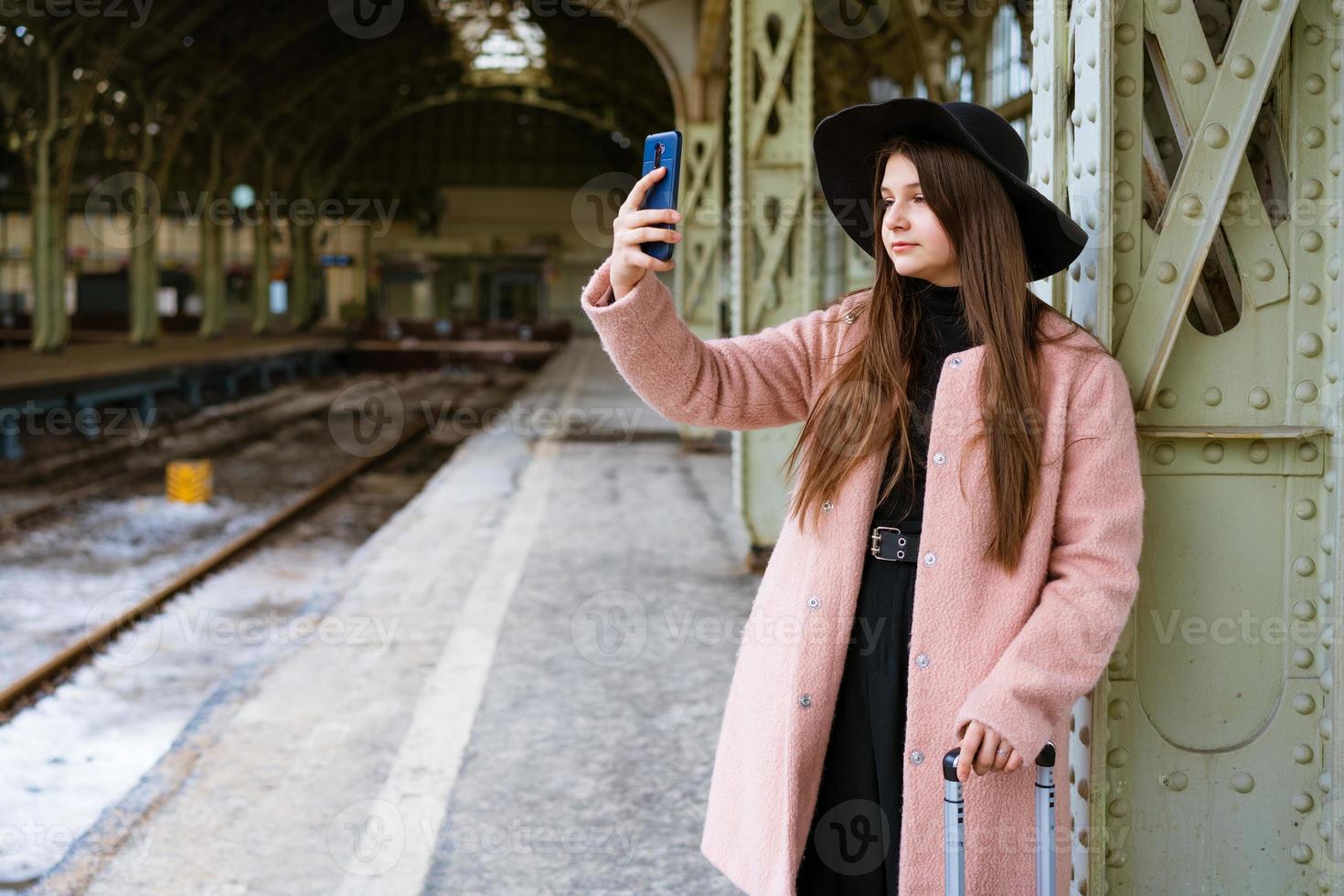 felice giovane donna sul binario della stazione ferroviaria in cappotto rosa e cappello nero foto