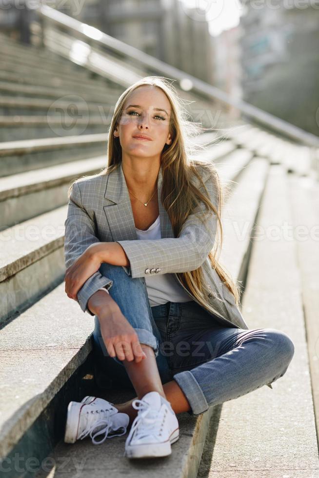 bella giovane donna bionda seduta sui gradini urbani. foto