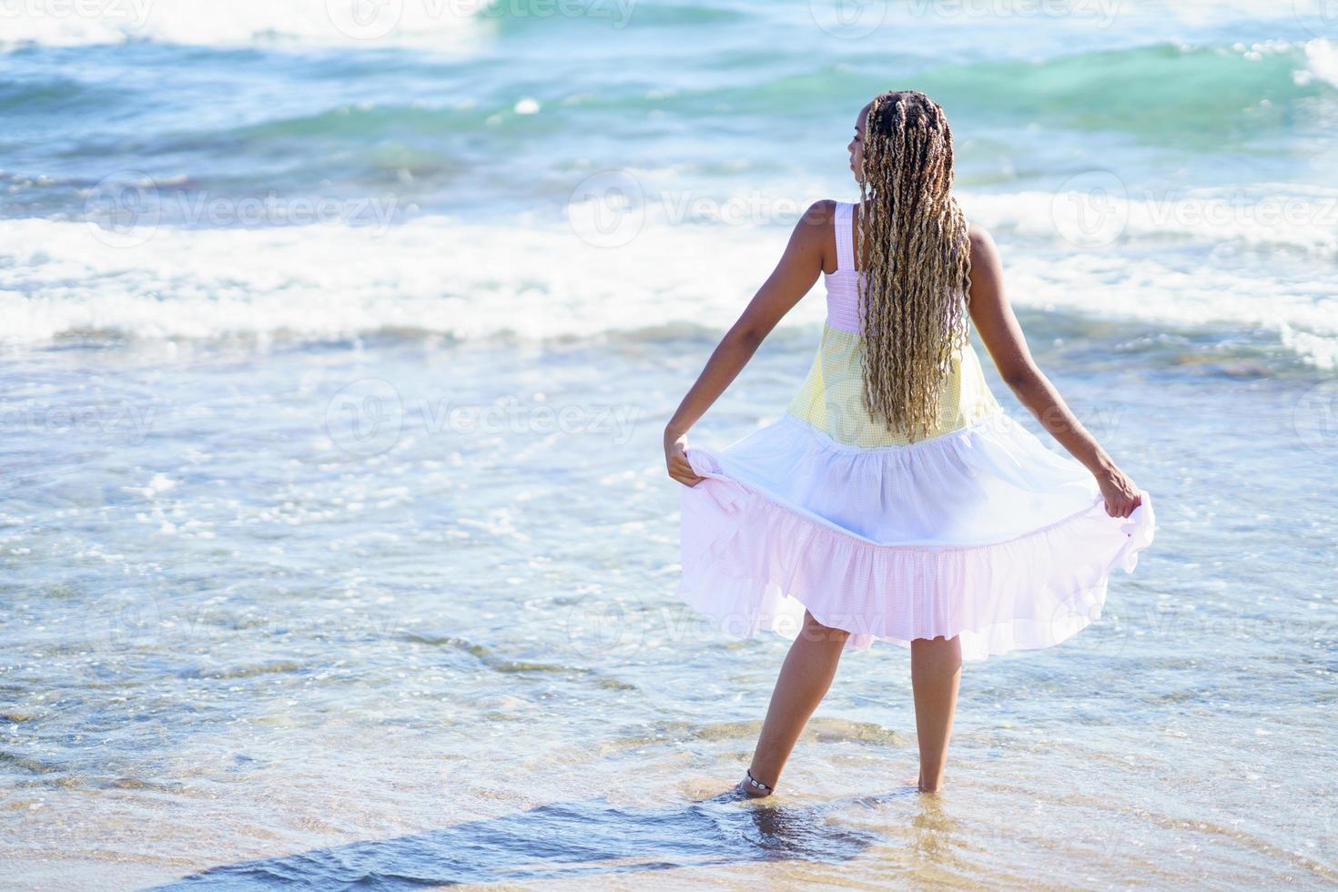 ragazza nera che cammina lungo la riva della spiaggia indossando un bellissimo abito lungo. foto