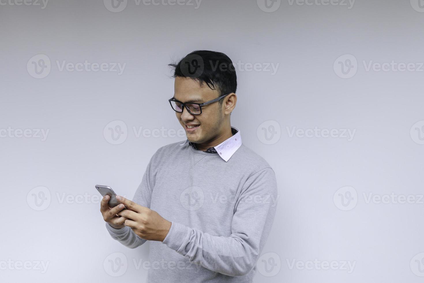 il giovane uomo asiatico intelligente è felice e sorridente quando utilizza lo smartphone in background foto