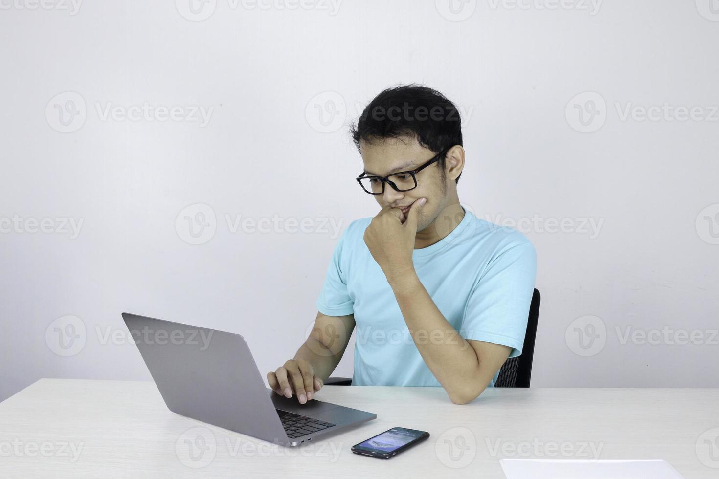 il giovane asiatico è serio e si concentra quando lavora su un laptop sul tavolo. uomo indonesiano che indossa una camicia blu. foto