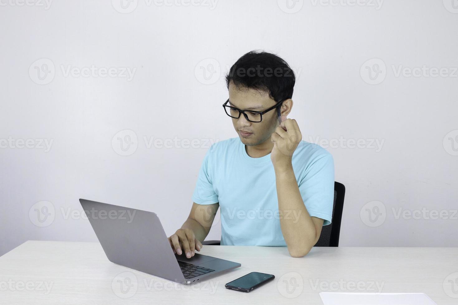 il giovane asiatico è serio e si concentra quando lavora su un laptop sul tavolo. uomo indonesiano che indossa una camicia blu. foto