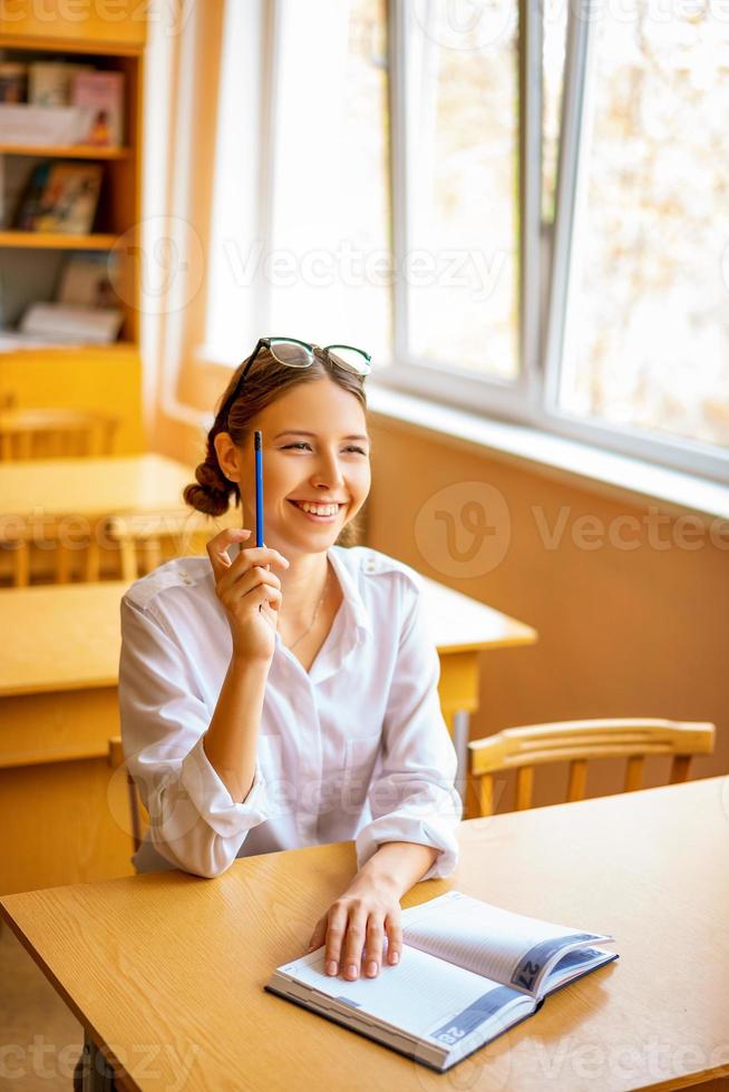 studente carino seduto con un taccuino alla scrivania vicino alla finestra, vista premurosa foto