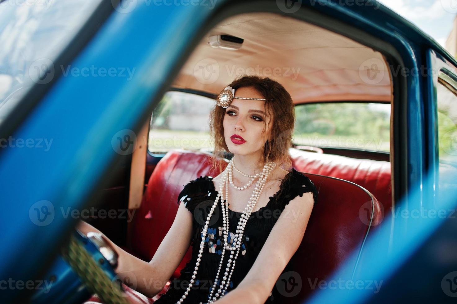 ritratto di bella modella riccia ragazza di moda con trucco luminoso in stile retrò seduto su un'auto d'epoca foto