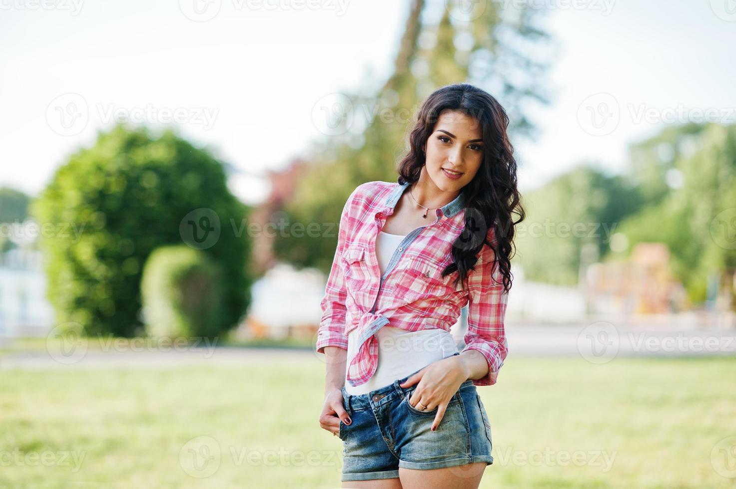 ritratto di ragazza di campagna in stile su pantaloncini di jeans corti e camicia a scacchi crosscountry foto