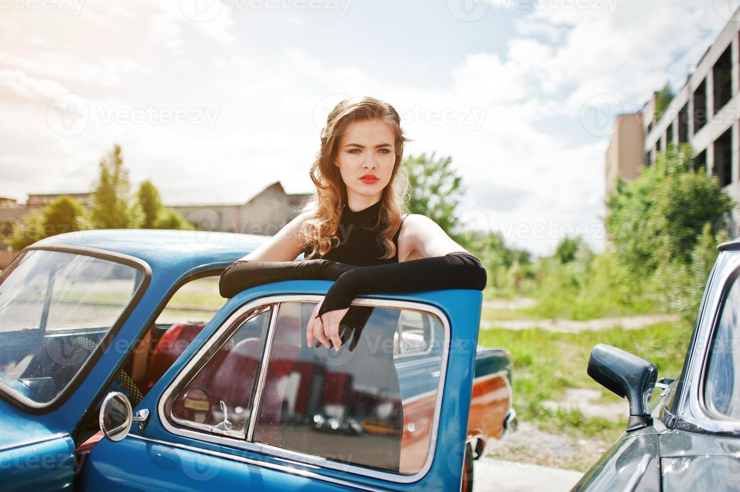 ritratto di bella ragazza di moda modello con trucco luminoso in stile retrò appoggiato su una portiera di un'auto d'epoca. foto