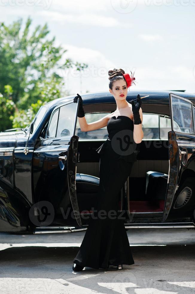 Ritratto di modello di bella ragazza di moda bruna sexy con trucco luminoso in stile retrò vicino a un'auto d'epoca con una sigaretta in mano. foto