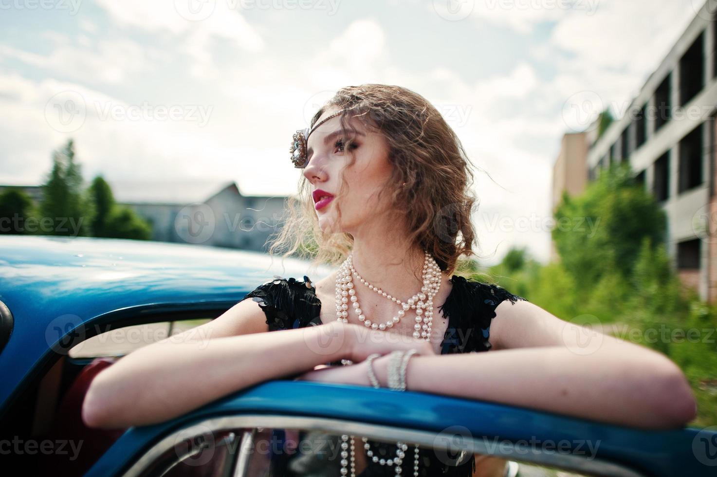 ritratto di bella modella riccia ragazza di moda con trucco luminoso in stile retrò appoggiato su una portiera di un'auto d'epoca. foto