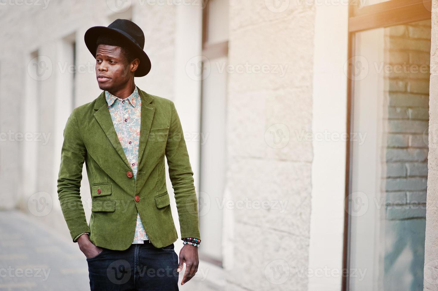 primo piano ritratto di moda di uomo afroamericano nero su giacca di velluto verde e cappello nero che cammina per le strade dello sfondo della città casa con molte finestre foto