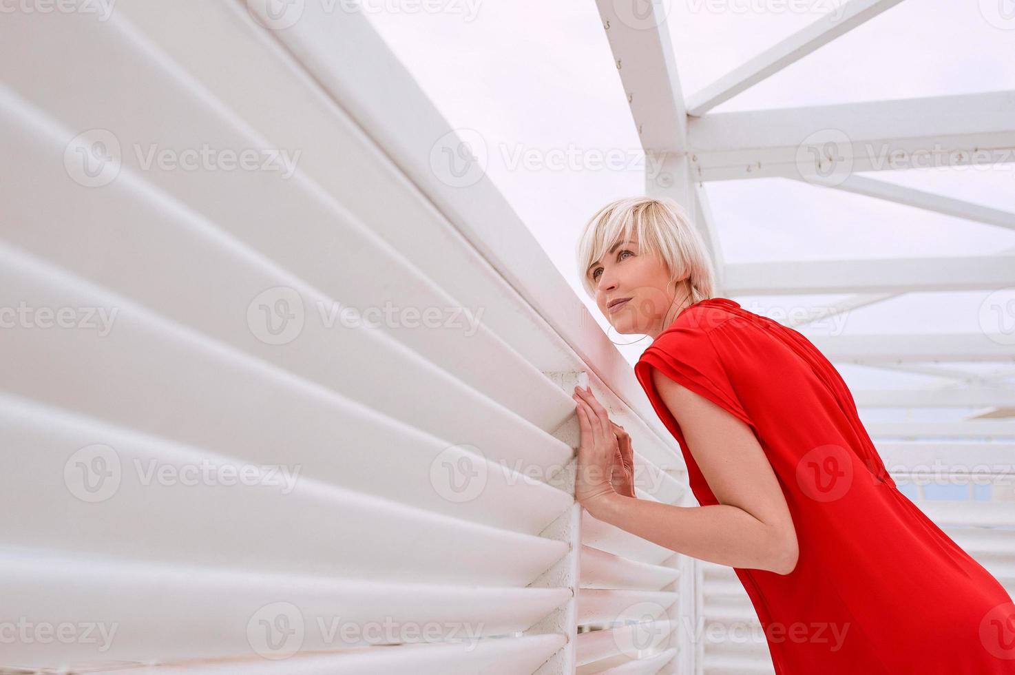 ritratto di bella donna bionda capelli corti piuttosto cool in abito di corallo rosso vicino a pergolato in legno bianco per la spiaggia foto