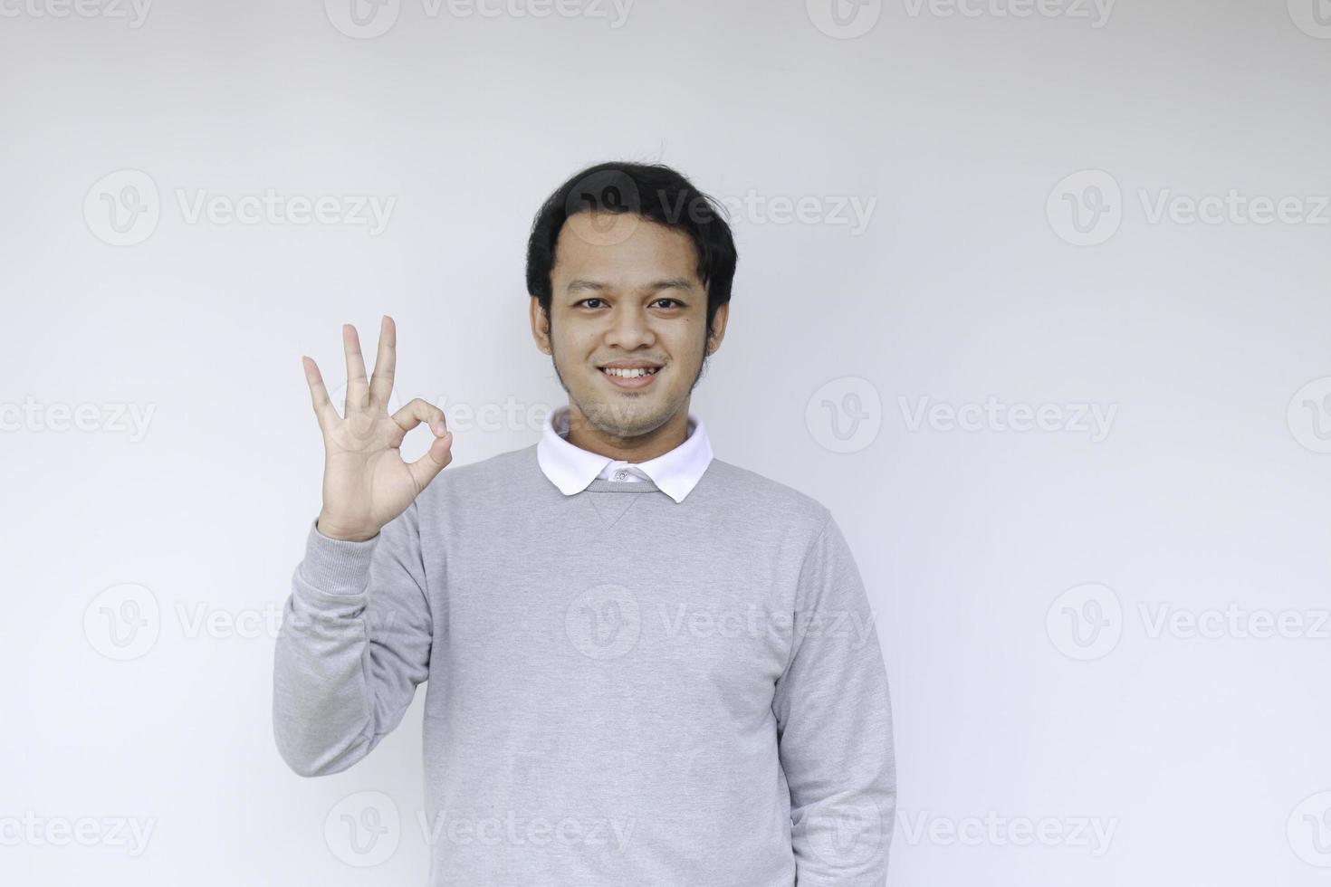 il giovane uomo asiatico indossa una camicia grigia con la faccia sorridente felice e il pollice in alto o il segno ok foto