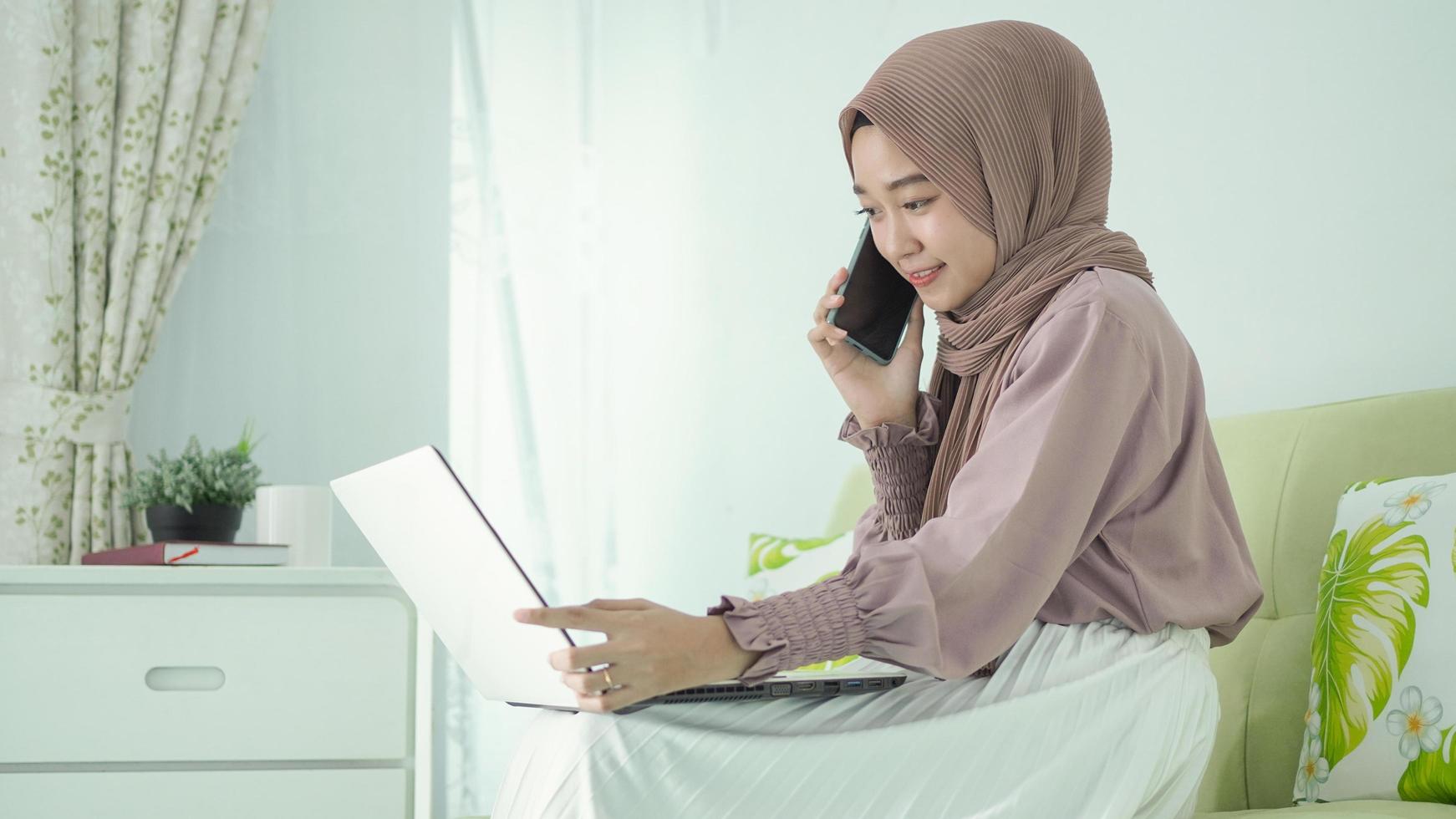 donna asiatica in hijab online a casa che discute tramite cellulare foto