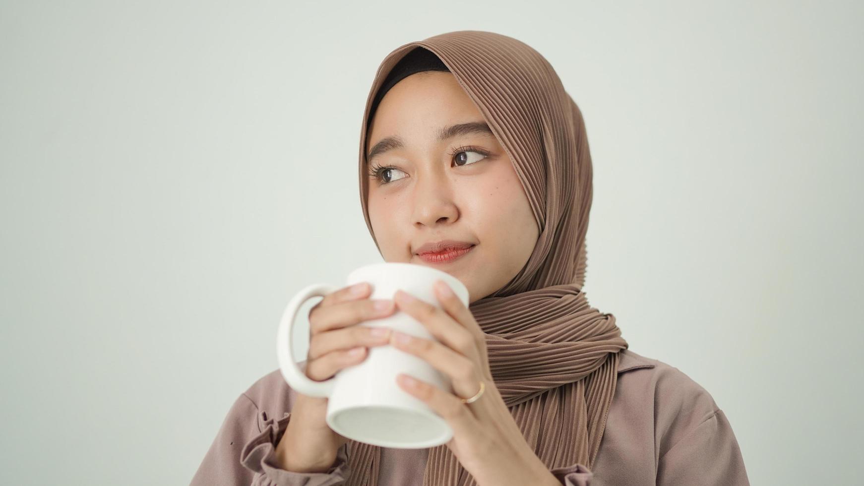 donna asiatica in hijab pensando all'ispirazione mentre si gusta un drink a casa foto