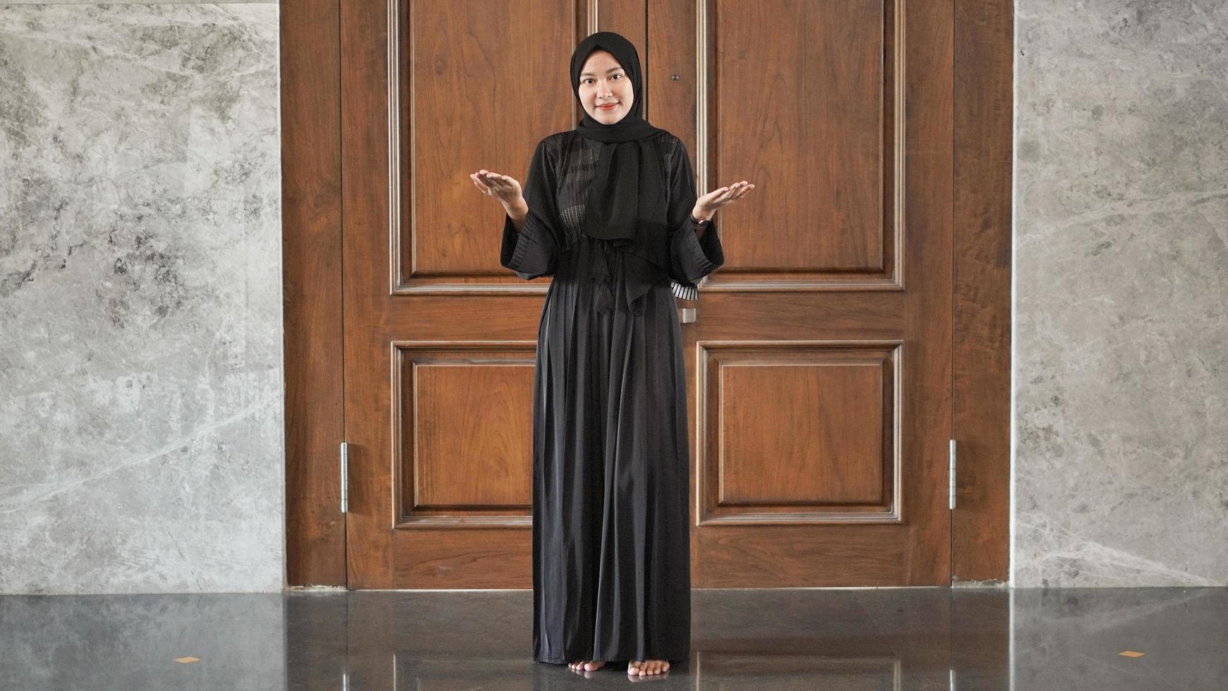 donna in abito musulmano nero che segnala il benvenuto alla porta foto