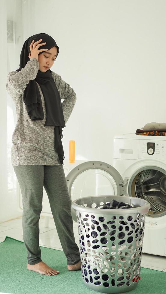 giovane donna asiatica vertigini guardando cesto di vestiti sporchi a casa foto