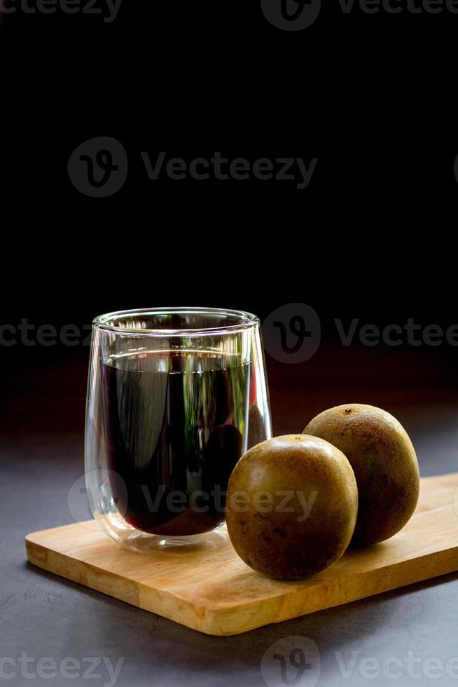 concetto di succo di erbe cinesi. succo di frutta arhat in un bicchiere con frutta arhat su un tagliere di legno su sfondo nero. foto