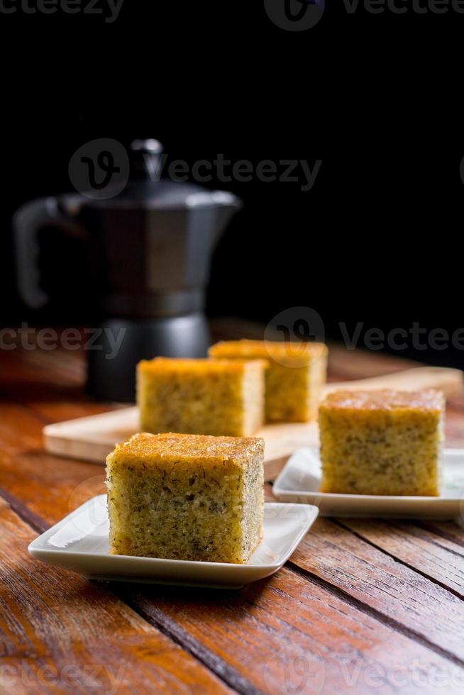 primo piano taglio quadrato di torta fatta in casa dolce e solf banana su piatto bianco sul tavolo con pentola moka nera solf focus. pasticceria deliziosa e sana. foto