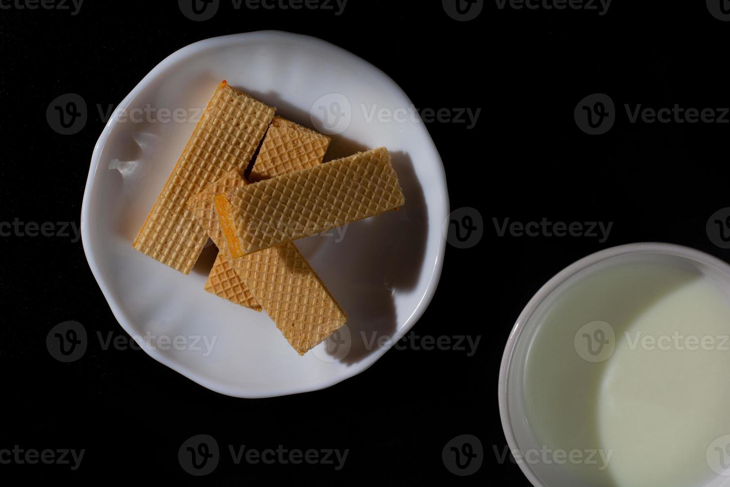 vista dall'alto quattro wafer in un piatto bianco con una tazza di latte su sfondo nero con spazio per la copia. foto