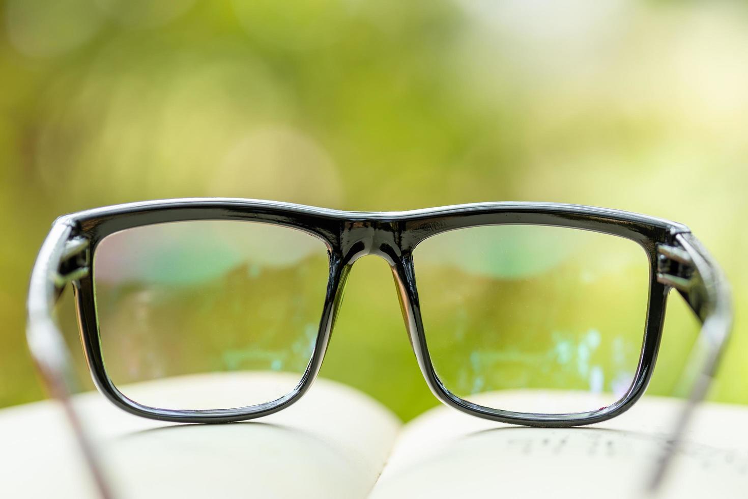 libro e occhiali su tavola di legno con natura verde astratta sfocatura dello sfondo. concetto di lettura e educazione foto