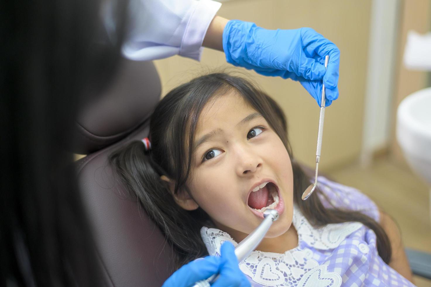 una piccola ragazza carina che ha i denti esaminati dal dentista in clinica dentale, controllo dei denti e concetto di denti sani foto