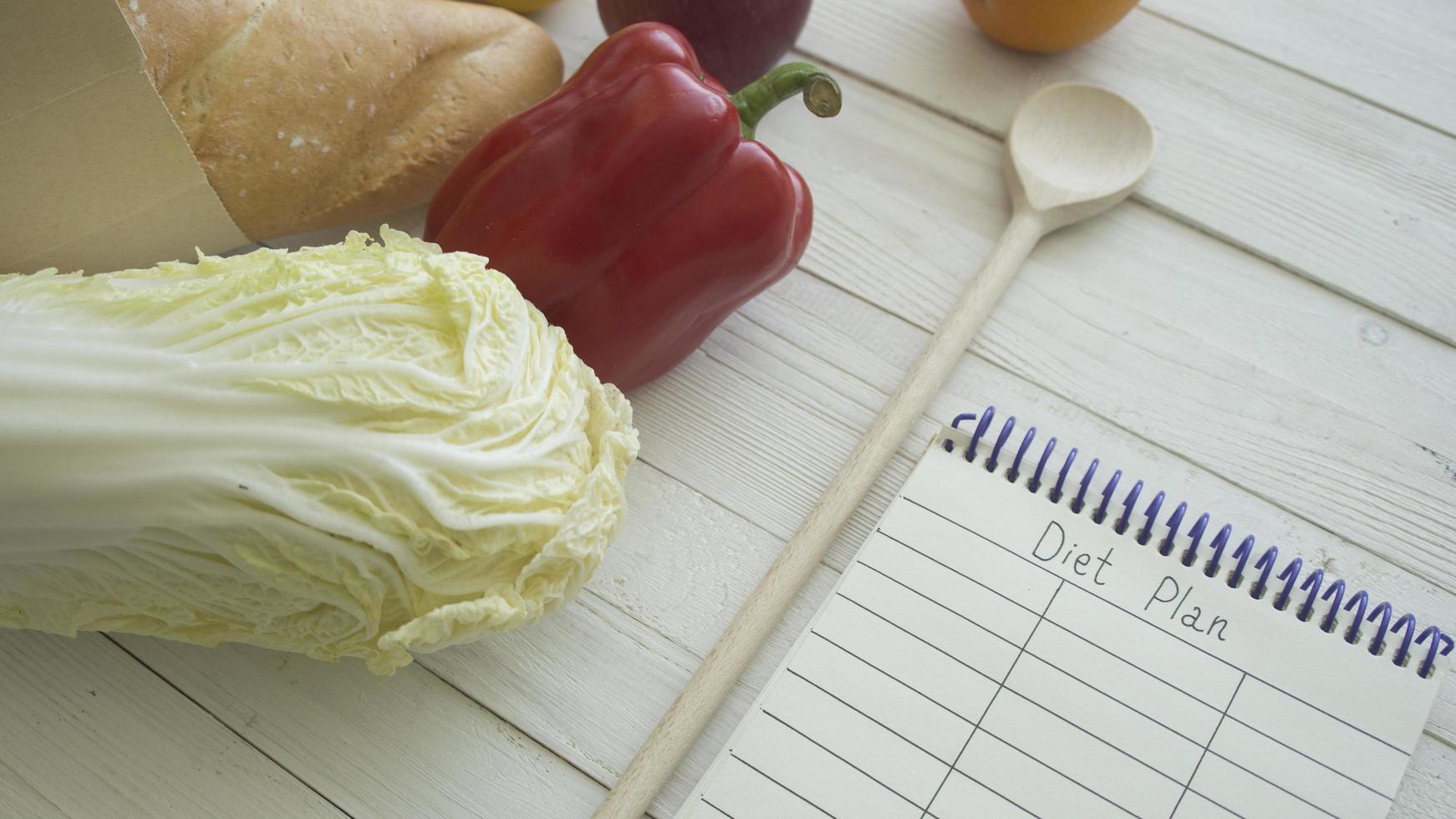 sacchetto di carta pieno di prodotti alimentari con piccolo taccuino vuoto su tavola di legno, vista dall'alto foto