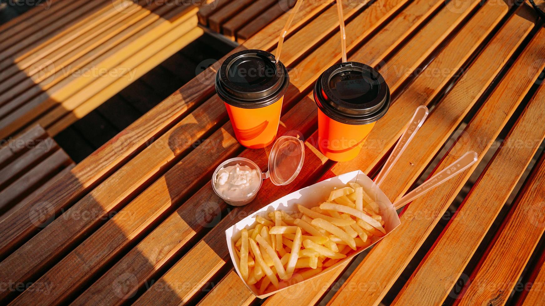 Fast food. due bicchieri di carta arancione e patatine fritte con salsa sul tavolo di legno foto