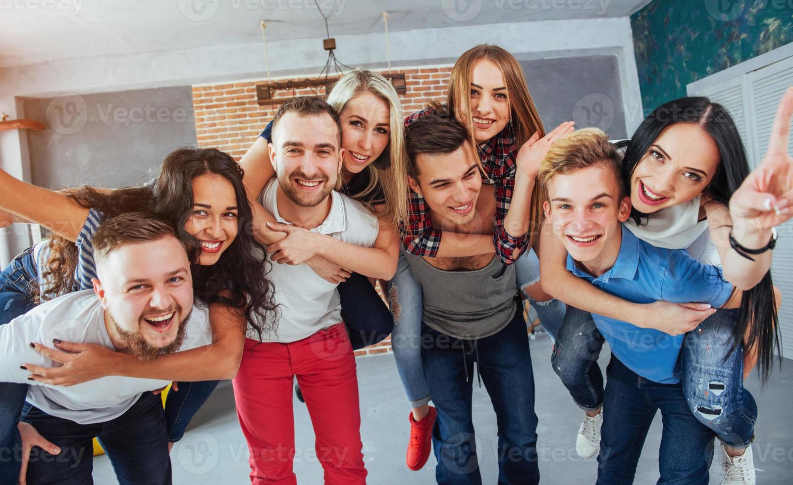 ritratto di gruppo di ragazzi e ragazze multietnici con abiti colorati alla moda che tengono un amico in posa su un muro di mattoni, persone in stile urbano che si divertono, concetti sullo stile di vita insieme giovanile foto