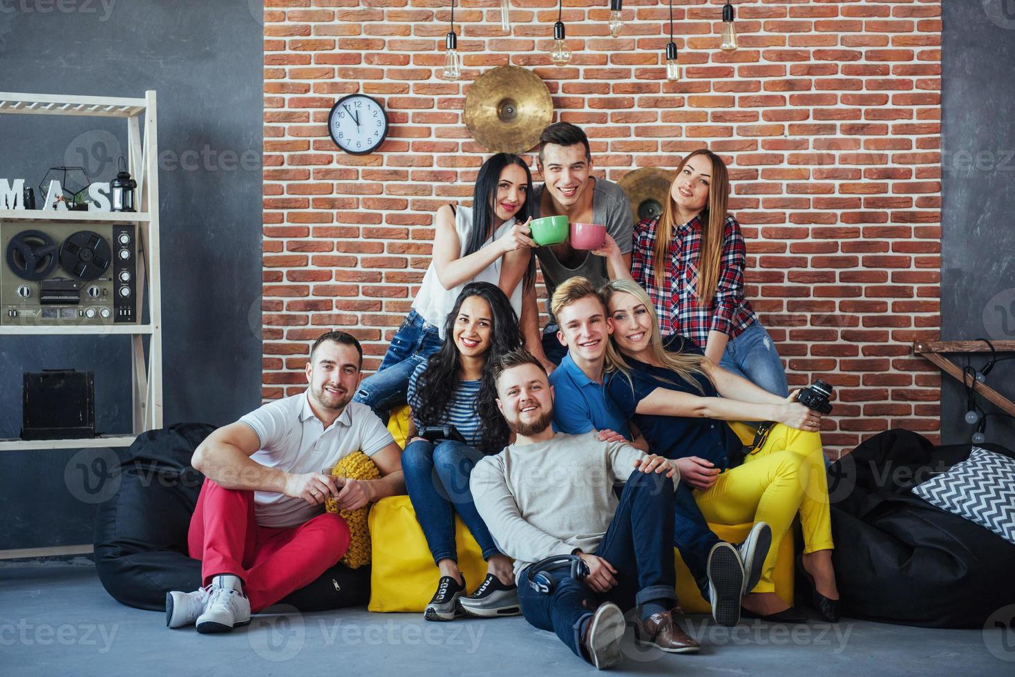 ritratto di gruppo di ragazzi e ragazze multietnici con abiti colorati alla moda che tengono un amico in posa su un muro di mattoni, persone in stile urbano che si divertono, concetti sullo stile di vita insieme giovanile foto