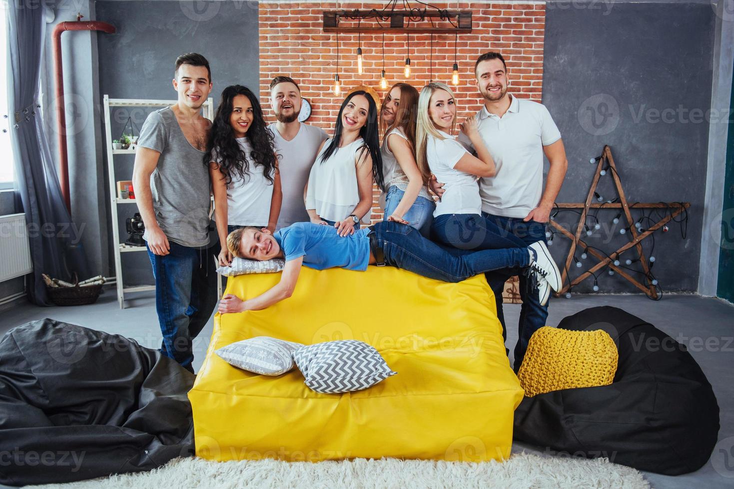 ritratto di gruppo di ragazzi e ragazze multietnici con abiti colorati alla moda che tengono un amico in posa su un muro di mattoni, persone in stile urbano che si divertono, concetti sullo stile di vita insieme giovanile foto