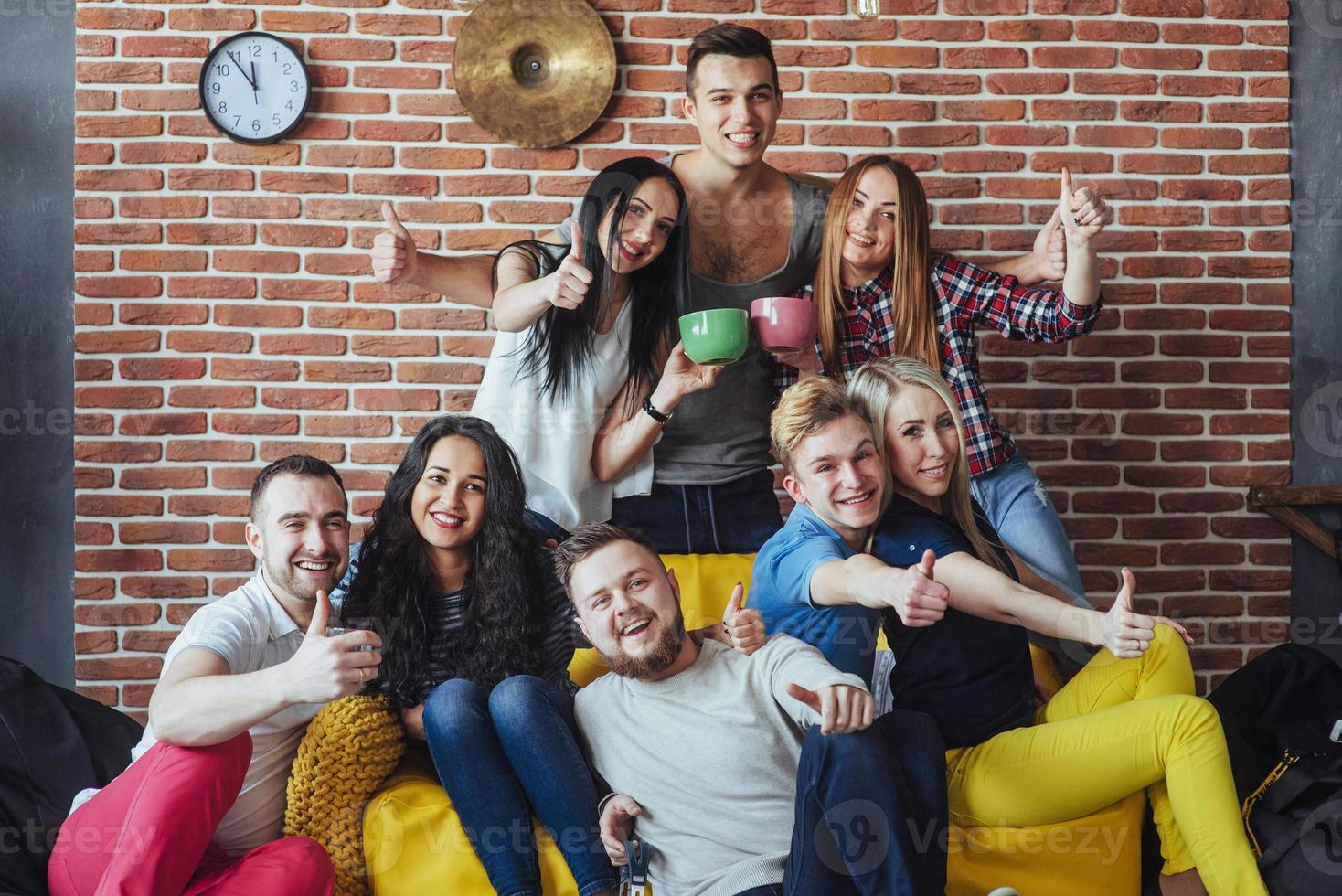 ritratto di gruppo di ragazzi e ragazze multietnici con abiti colorati alla moda che tengono un amico in posa su un muro di mattoni, persone in stile urbano che si divertono, concetti sullo stile di vita insieme giovanile foto