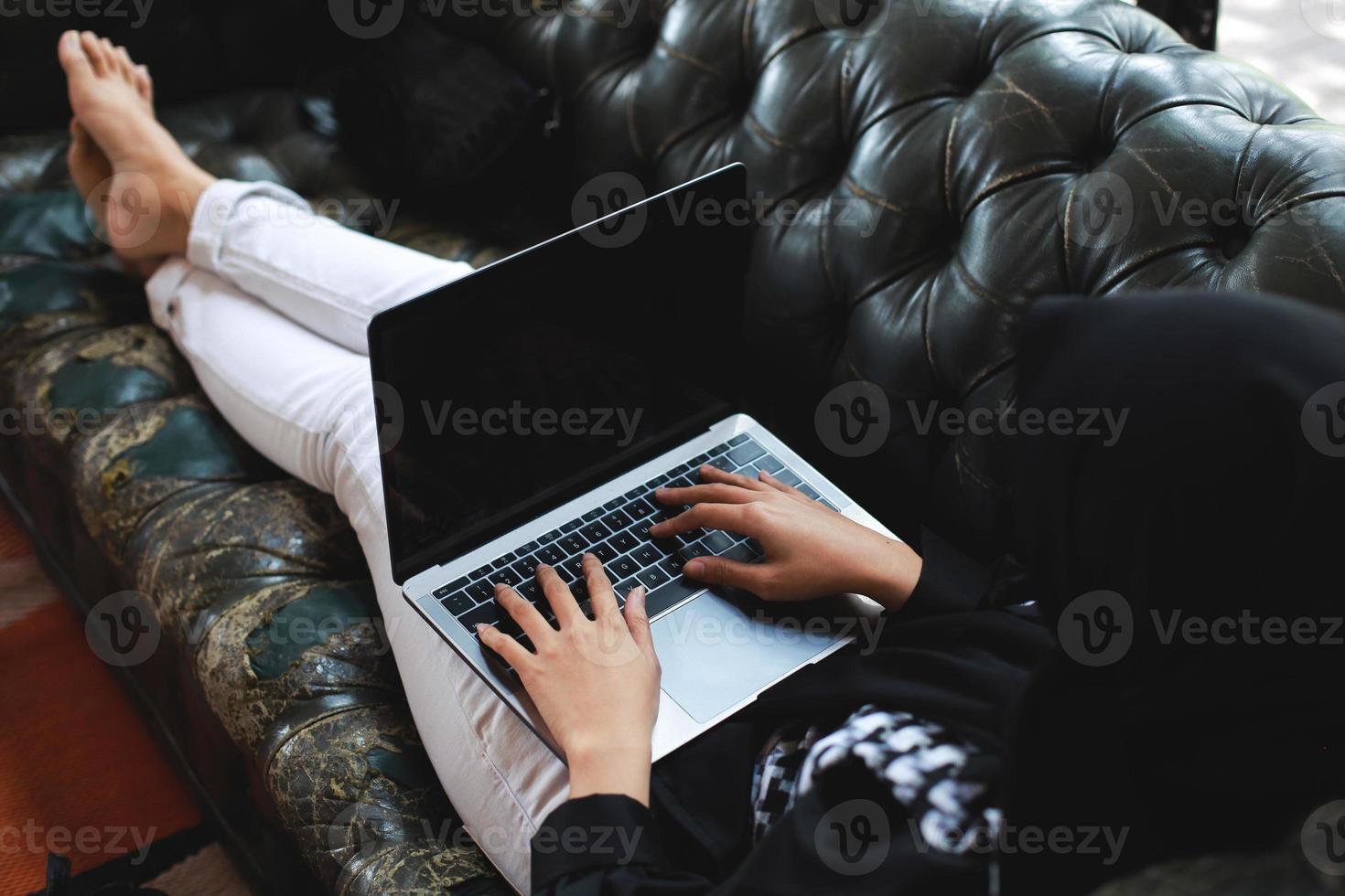 donna che si rilassa sul divano e digita sul computer portatile foto