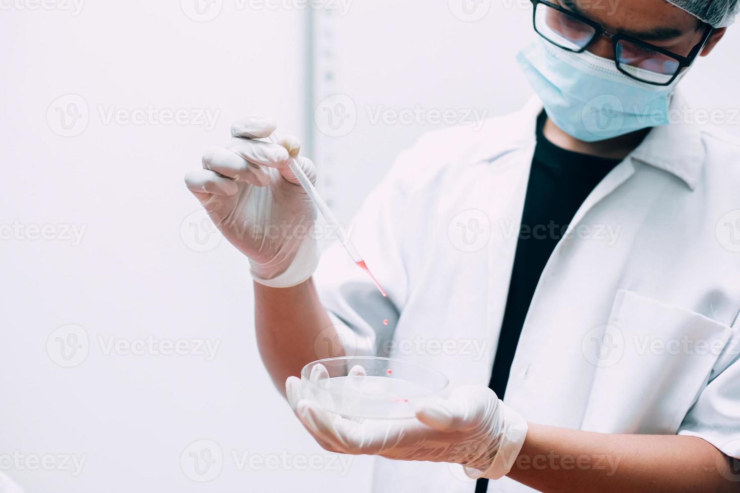 scienziato che tiene una pipetta e fa cadere un campione in una capsula di Petri foto