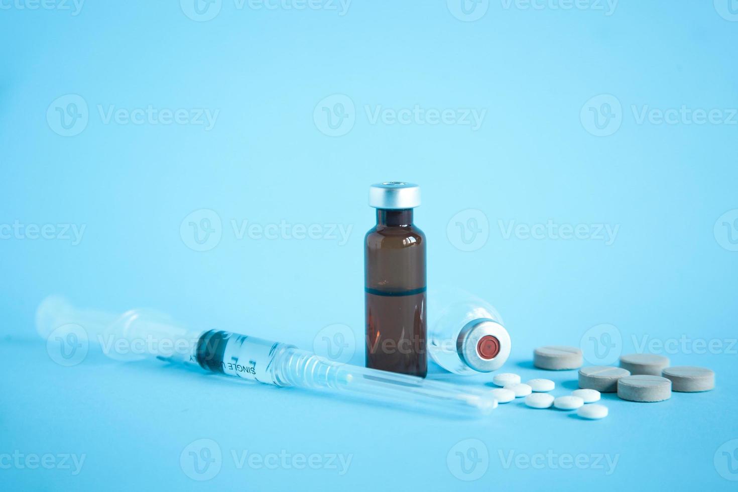 primo piano di una fiala di medicinale e vaccino con siringa e compressa su sfondo blu foto