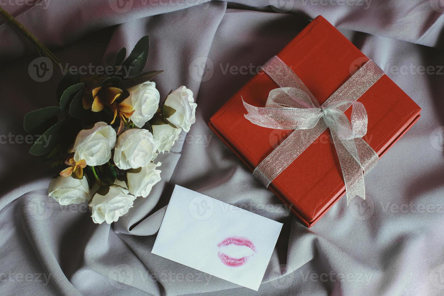 rose bianche con segno di bacio sulla busta e confezione regalo su panno grigio stropicciato foto