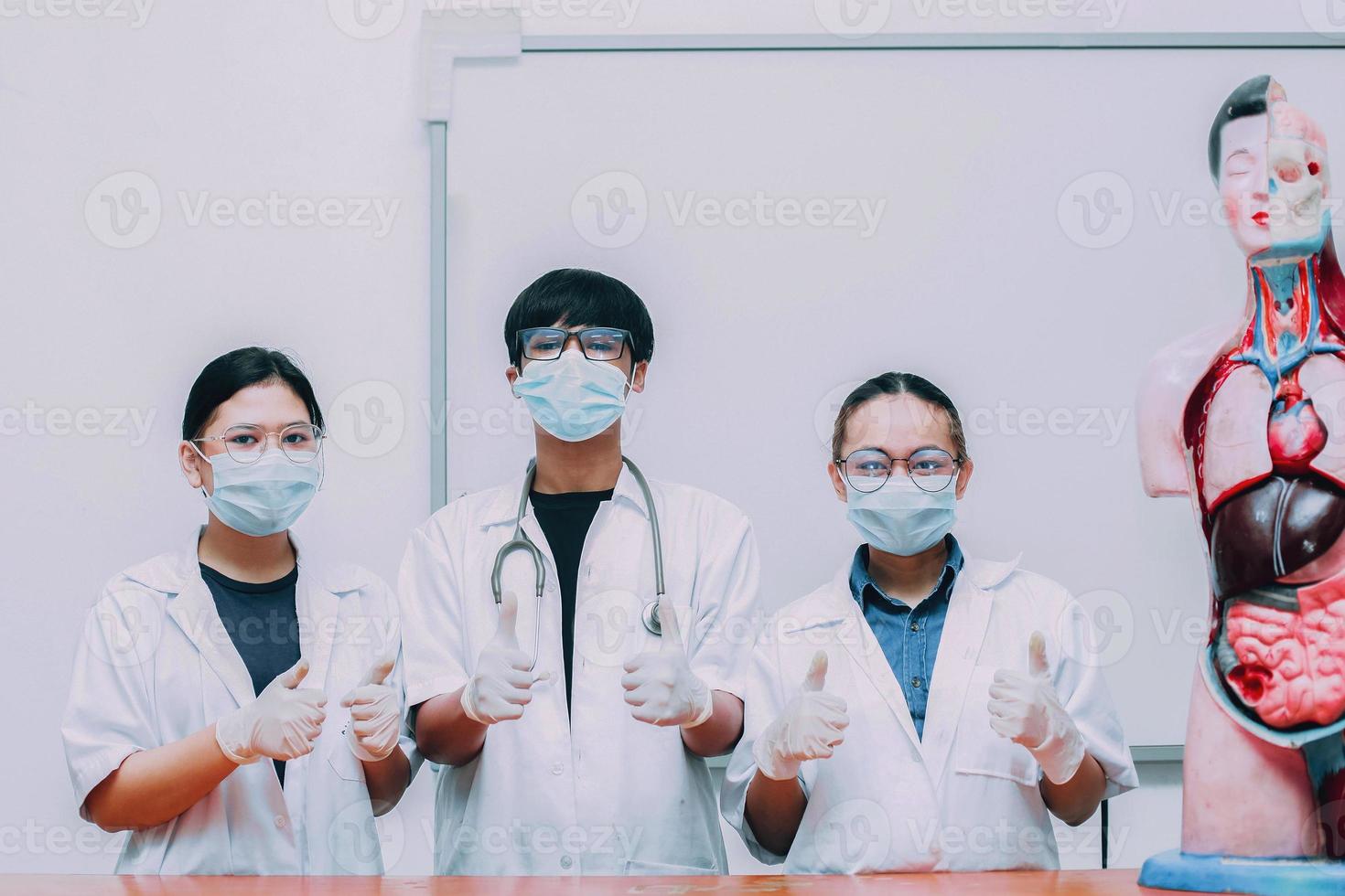 gruppo di giovane medico che indossa maschera protettiva e uniforme con il pollice in posa foto