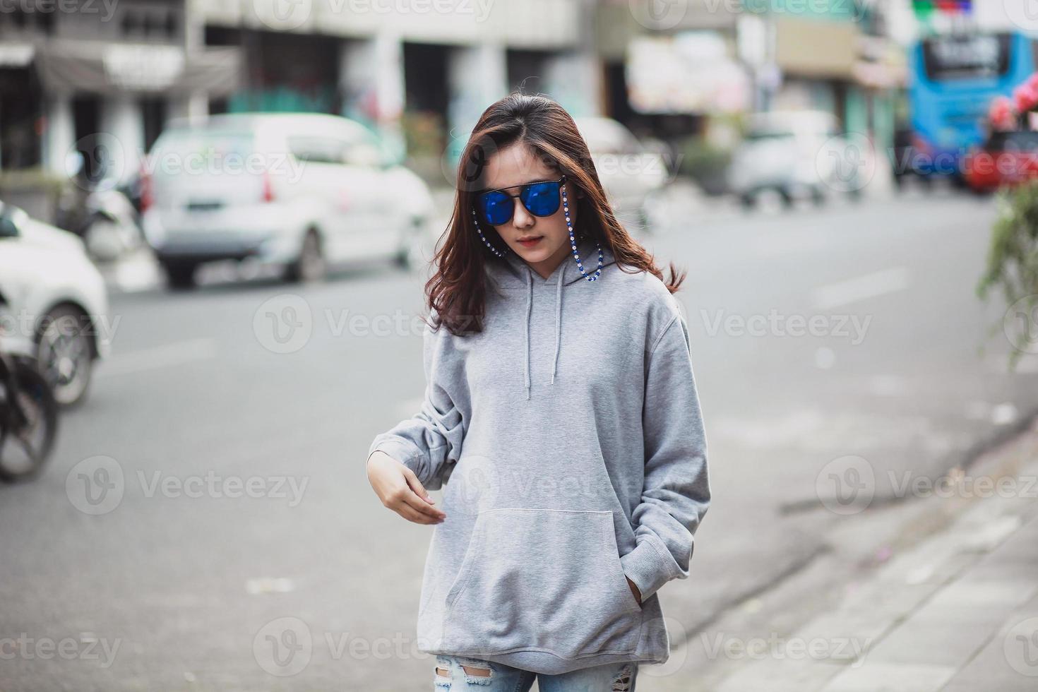 bella donna che indossa un maglione con cappuccio e occhiali da sole che cammina per la strada della città foto