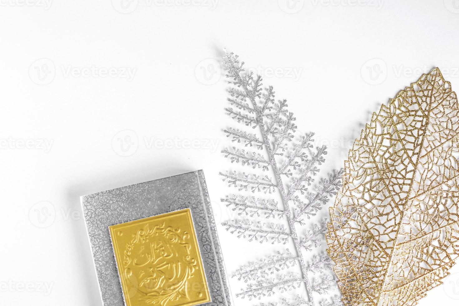 arabo piatto d'oro sul libro del sacro corano con foglie d'argento e d'oro su sfondo bianco foto
