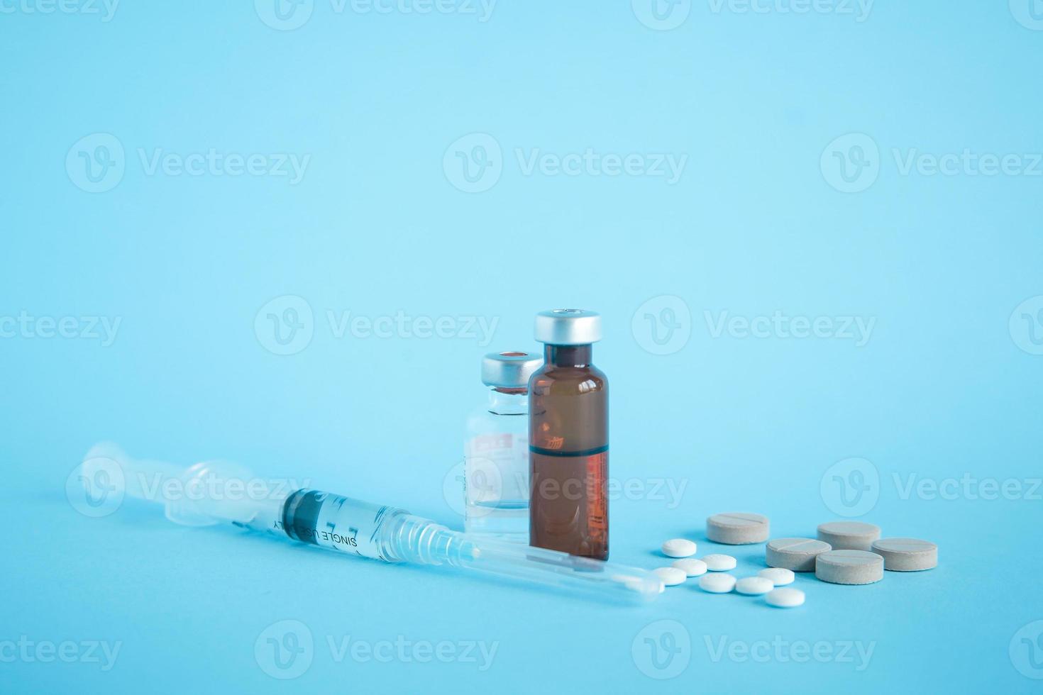 primo piano di una fiala di medicinale e vaccino con siringa e compressa su sfondo blu foto