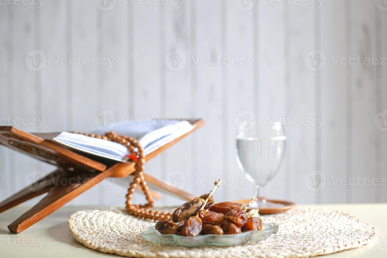 kurma o datteri frutta con bicchiere d'acqua, libro sacro al-quran e grani di preghiera sul tavolo. ramadan tradizionale, pasto iftar. concetto del mese di digiuno del ramadan kareem foto