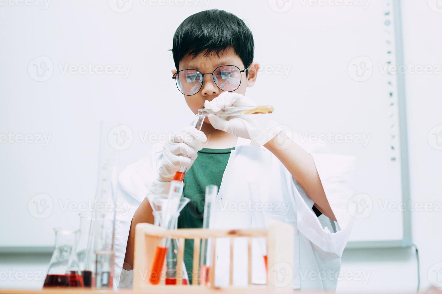 studente ragazzo asiatico con provette che studia chimica al laboratorio scolastico, versando liquido. giornata nazionale della scienza, giornata mondiale della scienza foto