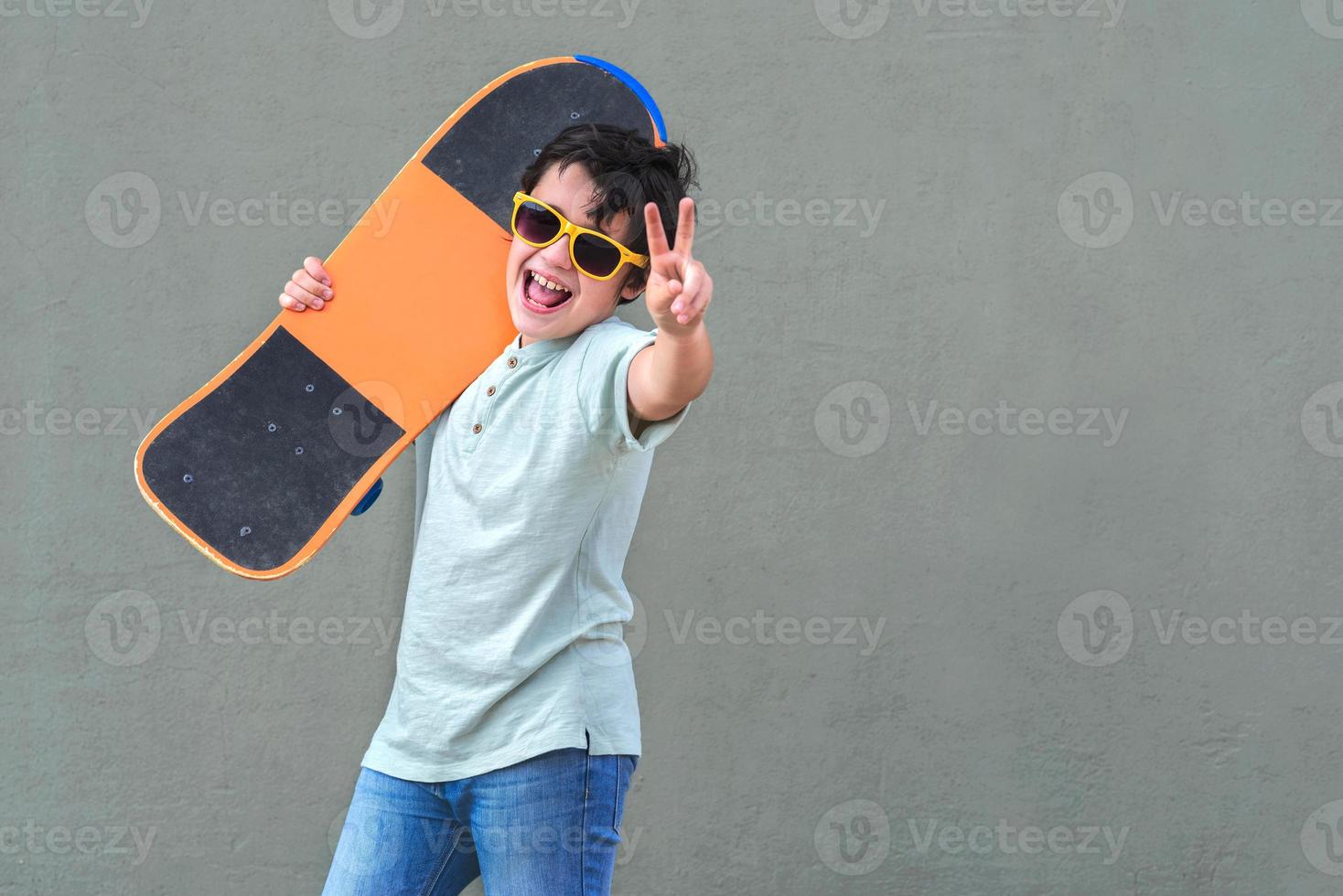 bambino felice e sorridente con skateboard e occhiali da sole per strada foto