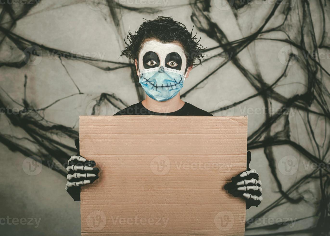 felice Halloween. bambino che indossa una maschera medica in un costume da scheletro che tiene una tavola marrone foto