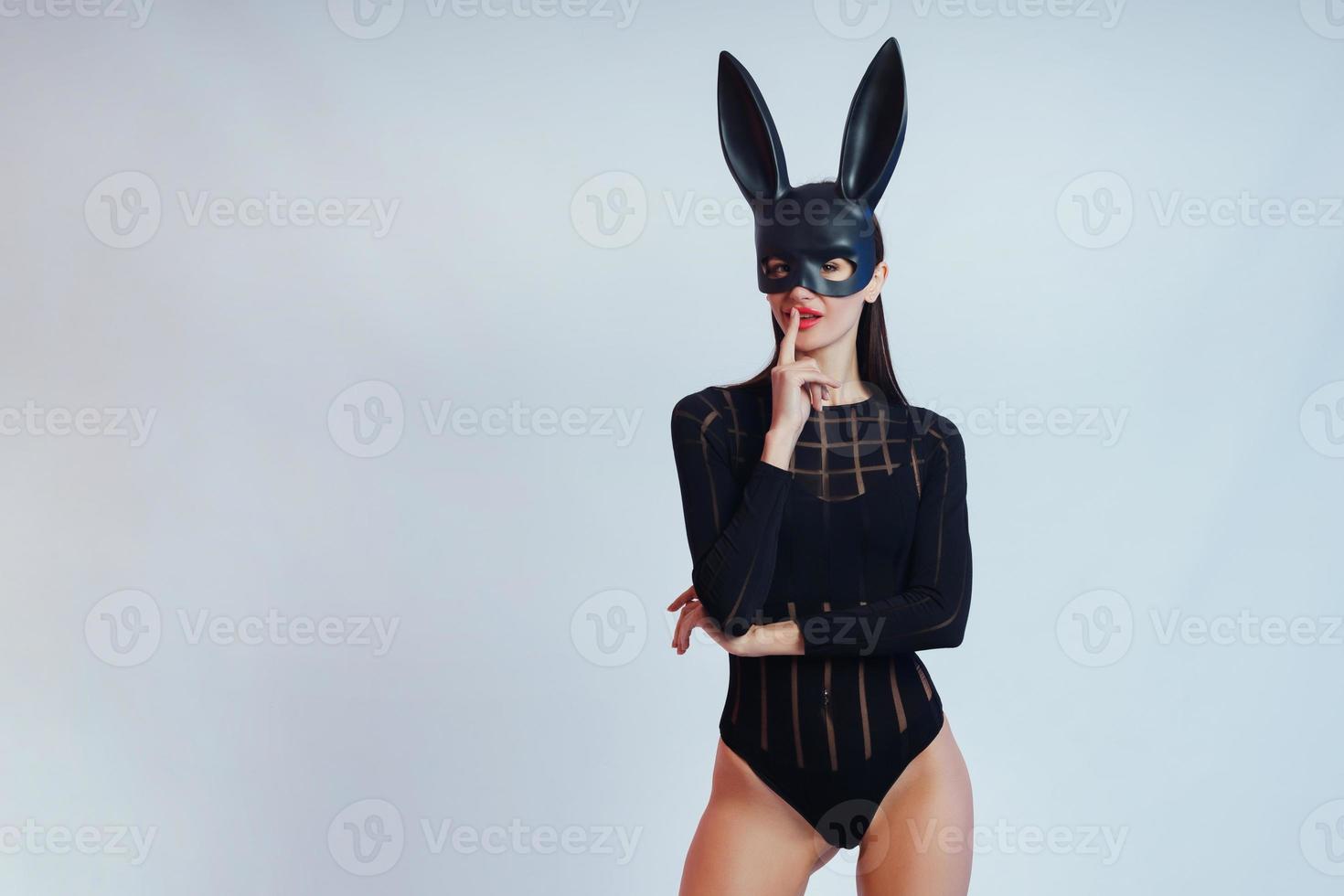 donna sexy che indossa un coniglietto di pasqua con maschera nera in piedi su uno sfondo blu e sembra molto sensuale foto