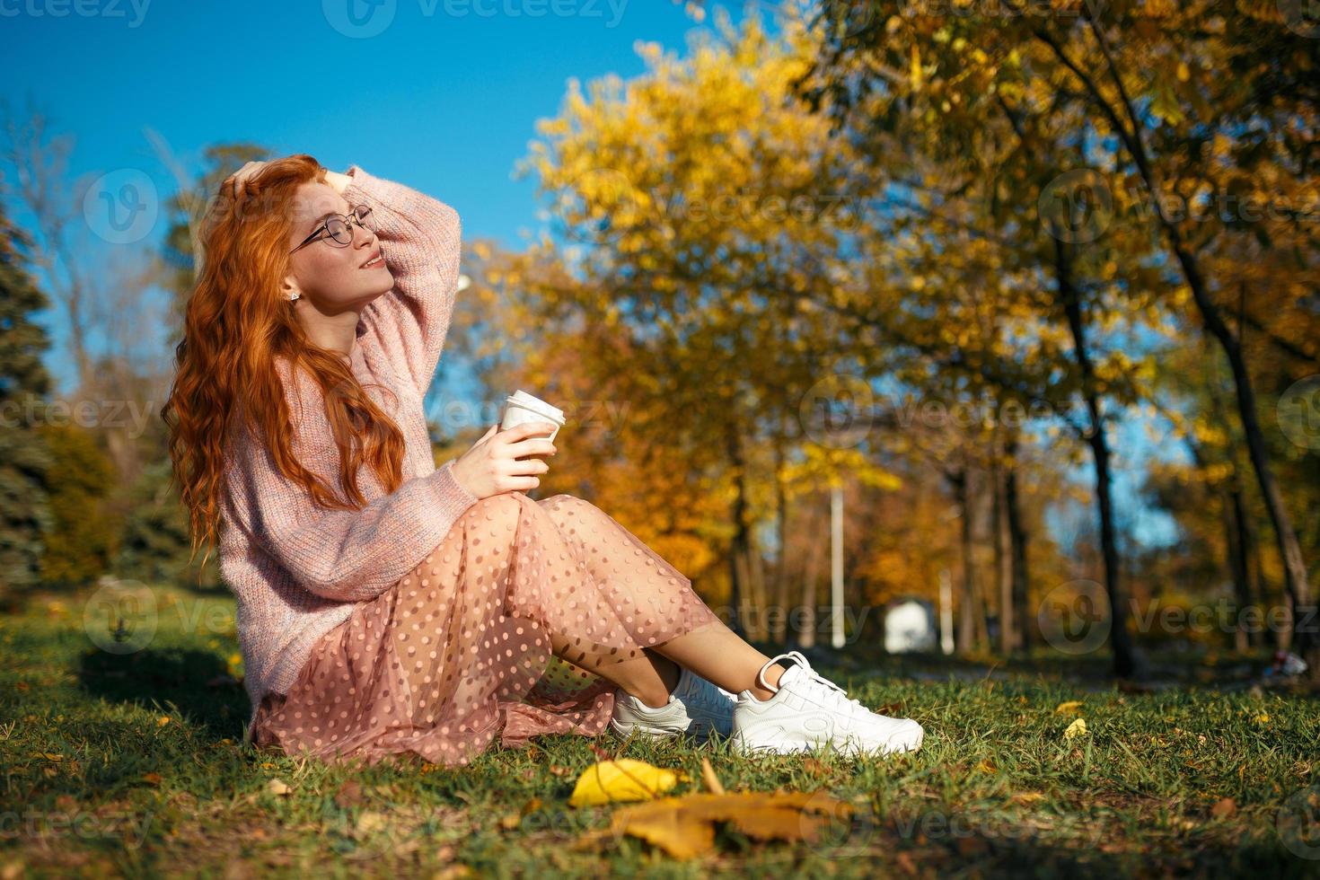 ritratti di un'affascinante ragazza dai capelli rossi con occhiali e un bel viso. ragazza in posa nel parco autunnale con un maglione e una gonna color corallo. foto