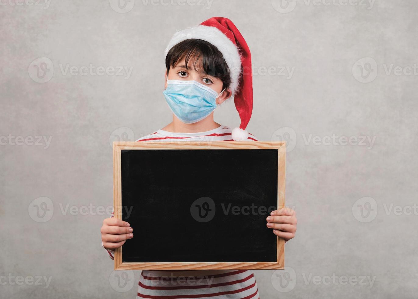 buon natale, bambino divertente con maschera medica che tiene una lavagna foto